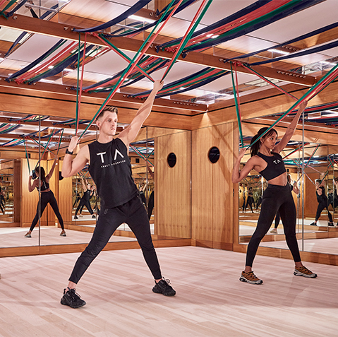 Two tracey anderson trainers stretch the resistance bands lining the ceiling