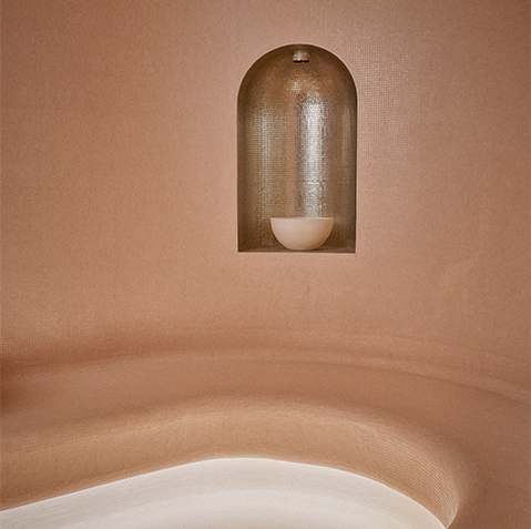 Pink curved walls of the steam room with a gold tiled shimmering niche